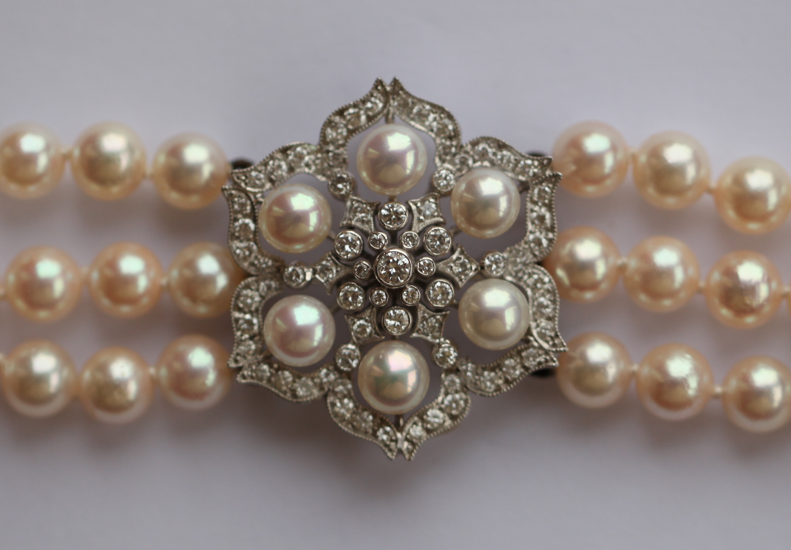 A three-row cultured pearl necklace with central diamond set floral cluster