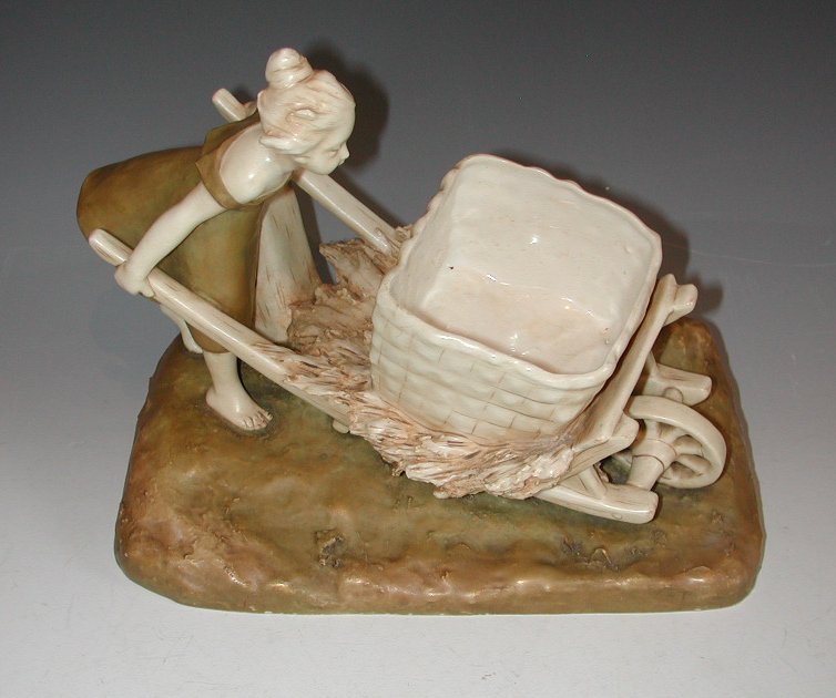 A Royal Dux figure group of a young girl pushing a wheel barrow