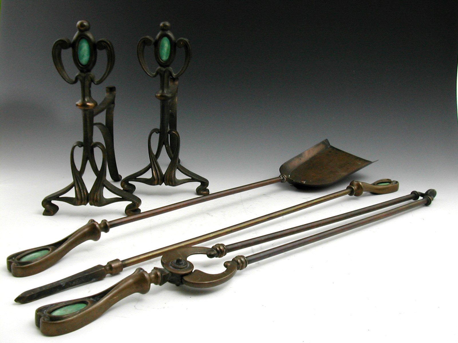 A pair of Art Nouveau copper alloy fire dogs and matching irons,