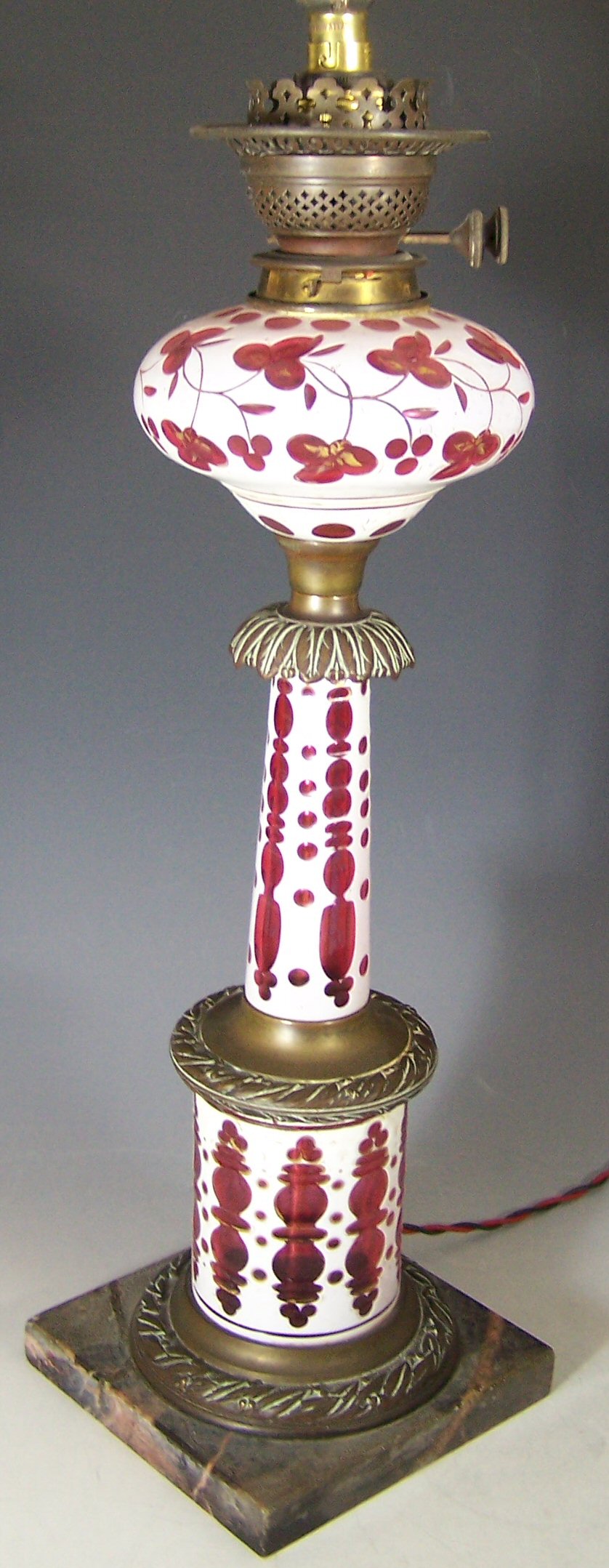 A white opaque and cased ruby glass and bronze oil lamp,