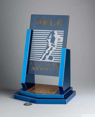 A trophy presented to Pelé composed of a blue tinted glass plaque etched with a stylized figure of a football player 
 and the caption "Pelé, Atleta d
