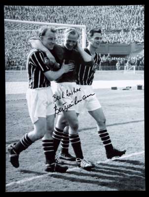 Bert Trautmann signed large photograph, 16 by 12in. b&w, being congratulated by team-mates and nursing his injured neck after the 1956 F.A. Cup Final,
