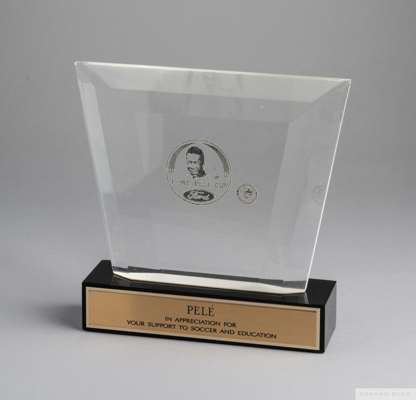 A trophy presented to Pelé composed of a clear acrylic plaque etched with a portrait of Pelé
 over the words "Ford/ Pelé Cup", mounted on a black acry