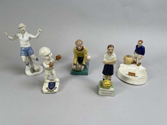 A crested Arcadian ash tray and match holder modelled as a Chelsea footballer, a continental figure of a footballer, another ceramic figure of a footb