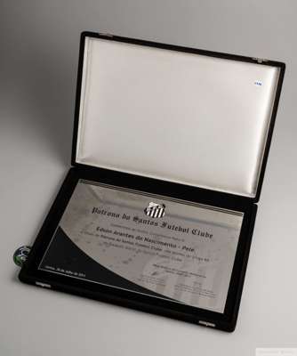 An engraved metal plaque, accompanied by an identical printed certificate, presented to Pelé by the board of the Santos Football Club. 
 "Patrono do S