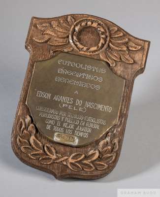 A gold tone base metal plaque, mounted on wood, presented to Pelé by the members of the Argentine Footballers Union. The plaque is inscribed (translat