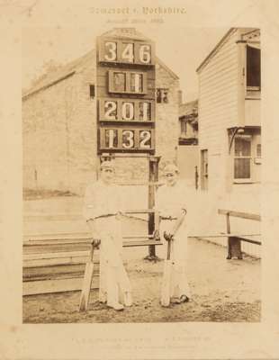 An original sepia toned photograph portraying L.C.H Palairet and H.T Hewett standing in front of the scoreboard on the occasion of their record, first